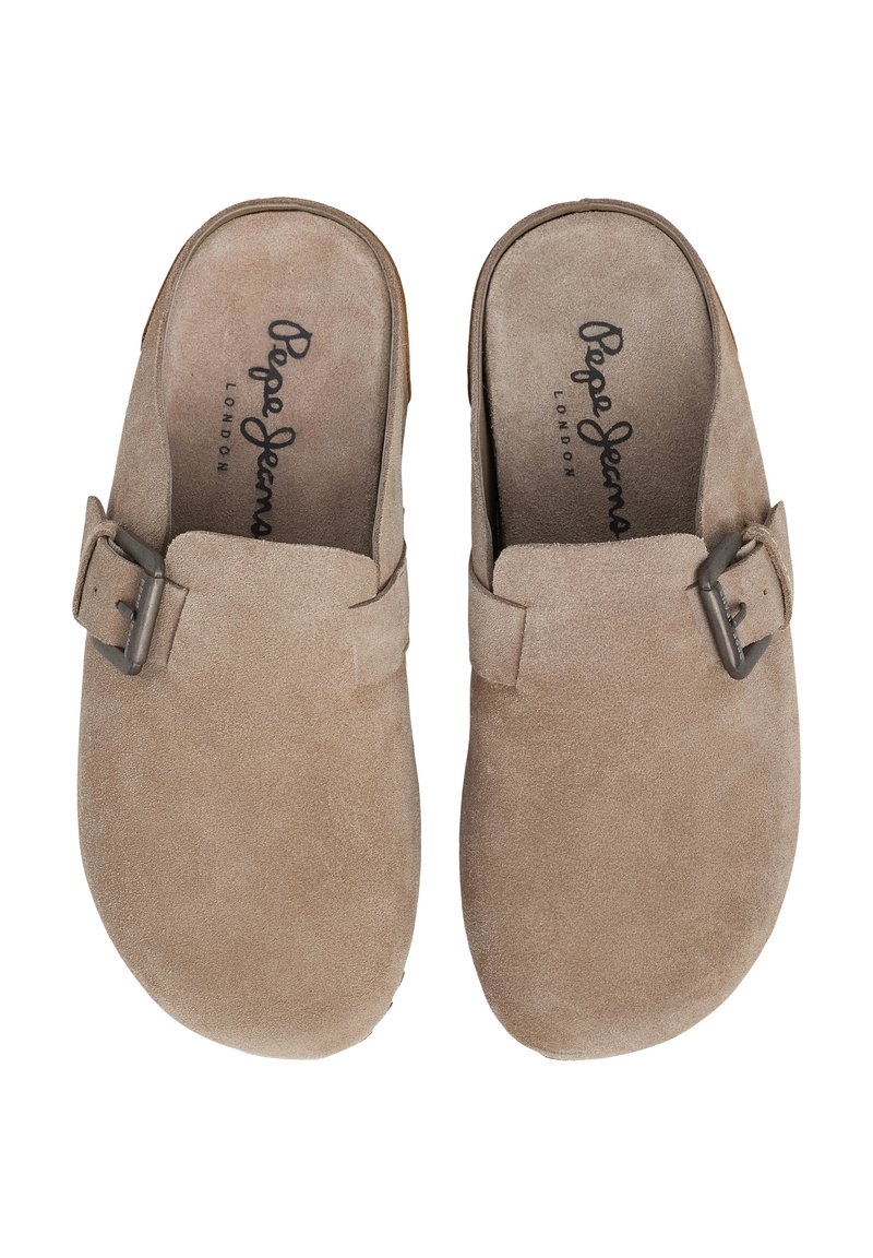 Mules en daim beige avec un embout rond, dotés d'un accent de boucle en métal et d'une semelle intérieure texturée. Semelle plate pour un enfilage facile.