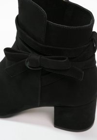 Bottine en daim noir avec talon bloc et nœud décoratif noué autour de la cheville.