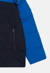 Padded jacket featuring a color-block design with a blue upper and navy lower section. Includes a zippered pocket on the side.