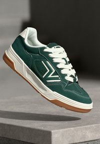 Grüne Wildledersneaker mit weißen Schnürsenkeln, einer weißen Gummisohle und einem Logo an der Seite. Sie verfügen über perforierte Details und genähte Akzente.
