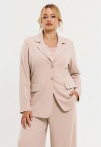 Lichtbeige blazer met een inzetkraag, twee knopen, voorzakken en een getailleerde pasvorm, gecombineerd met een satijnen top in een bijpassende tint.