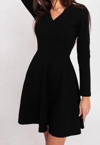Czarna sukienka z długim rękawem, z dekoltem w serek, dopasowanym gorsetem i rozkloszowanym dołem. Gładka tekstura i długość do kolan, z bocznymi kieszeniami.