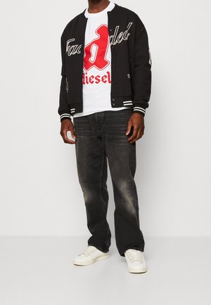 Sort varsityjakke med hvide accenter, rød grafisk t-shirt, mørke jeans og hvide sneakers. Jakken har broderede detaljer.