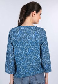 Blaue Bluse mit floralem Muster und dreiviertel Ärmeln, mit Rundhalsausschnitt und weichem Textilmaterial. Rückansicht angezeigt.