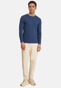 Langärmliges blaues T-Shirt in figurbetontem Design, aus strukturiertem Stoff. Kombiniert mit hellbeigen Hosen und sandfarbenen Sneakers für einen lässigen Look.