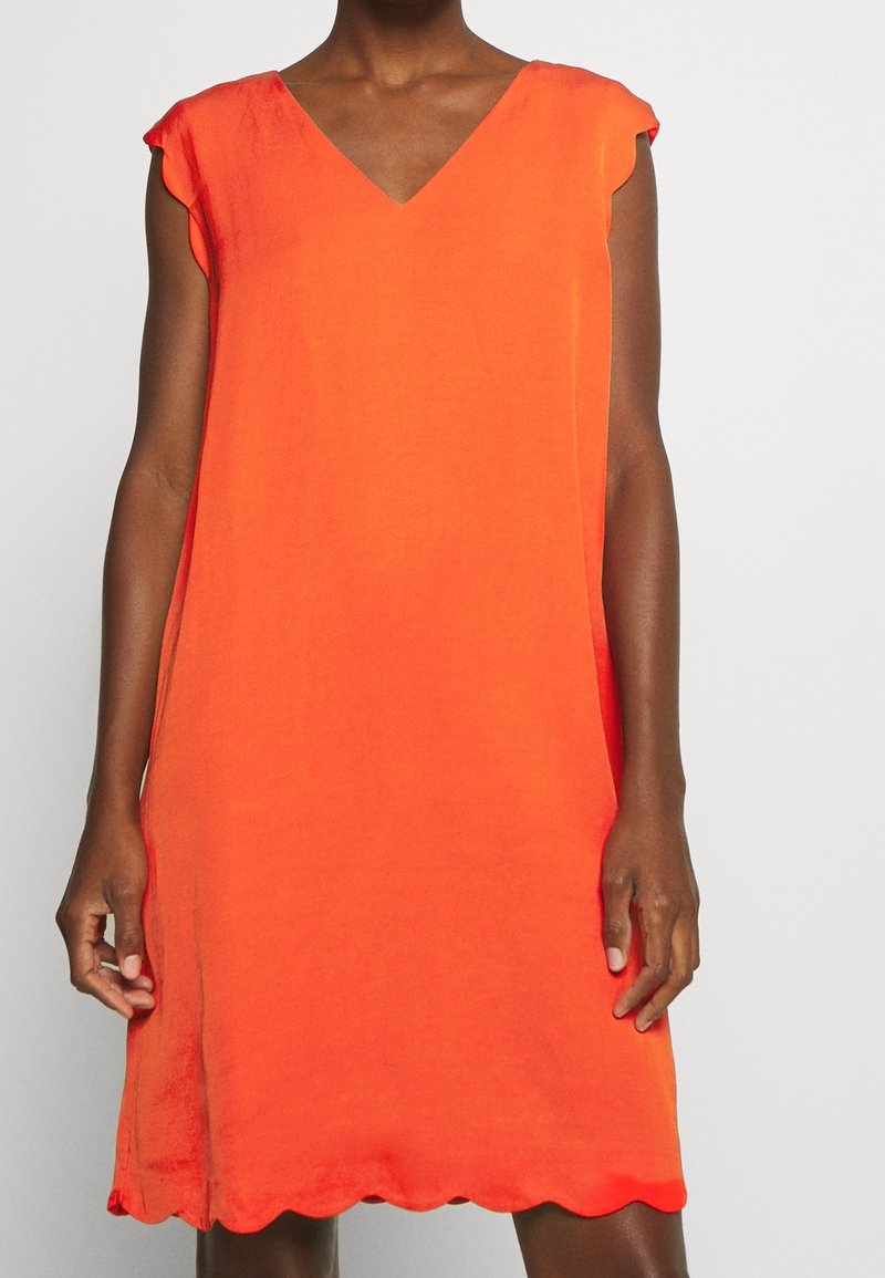 Oranje mouwloos jurkje met een V-hals, zachte textuur en gegolfde zoom. Lichtgewicht stof met een relaxte pasvorm.