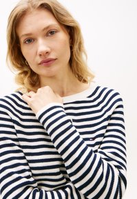 Πλεκτό πουλόβερ με ρίγες σε ναυτικό μπλε και λευκό, με στρογγυλή λαιμόκοψη και μακριά μανίκια. Ριμπ μανσέτες και μικρό λογότυπο στο στήθος.