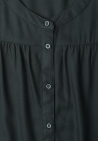 Blouse noire avec encolure arrondie, tissu froncé sous la poitrine et une rangée verticale de cinq petits boutons ronds au centre.