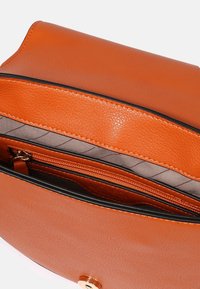 Borsa a mano in pelle marrone con una texture liscia, caratterizzata da un'apertura superiore, una tasca interna con zip e bordini neri a contrasto. Fodera interna di colore grigio.