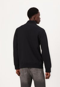 Pullover blu navy con colletto, maniche lunghe e polsini a coste. Realizzato in un tessuto morbido, presenta una vestibilità comoda e un design semplice.