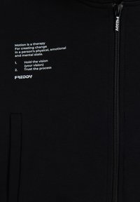 Felpa nera con zip realizzata in tessuto liscio, caratterizzata da testo bianco sul davanti che elenca frasi motivazionali e il nome del marchio "FREDDY."