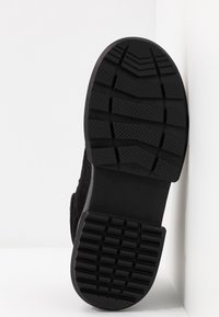 Suela de bota de ante negro con goma texturizada para agarre, que presenta un diseño de dibujo en relieve y una construcción robusta para mayor durabilidad.