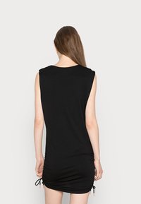 Vestido preto sem mangas com decote redondo, lados franzidos e laços ajustáveis na bainha. Tecido macio e suave com uma silhueta ajustada.