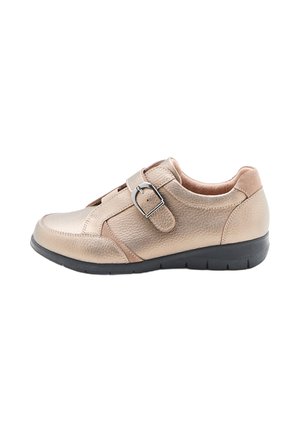 Zapato de cuero beige con un acabado texturizado, correa con hebilla ajustable, puntera redonda y suela de goma negra, presentando un diseño de perfil bajo.