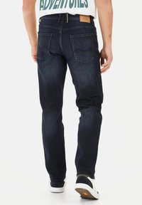 Donkerblauwe denim jeans met een rechte snit, vijf zakken, zichtbare stiksels en een tan leren label op de achterste tailleband.