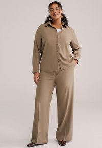 Bež srajca z gumbi, ovratnikom in dolgimi rokavi, kombinirana s širokimi bež hlačami. Gladek material, minimalističen dizajn in sproščen kroj.
