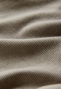Tessuto beige chiaro con sottili strisce verticali, che mostra una texture liscia e una leggera lucentezza. Le pieghe creano onde morbide nel materiale.