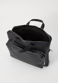 Sac en cuir noir avec deux zips, une poignée supérieure et un intérieur spacieux. Texture lisse et design minimaliste sans motifs visibles.