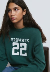 Suéter verde de punto con texto blanco "BROWNIE" y "22". Cuello redondo acanalado y corte relajado, con mangas largas y tejido texturizado.