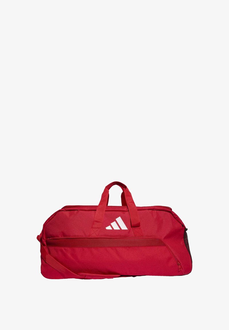 Bolsa de deporte roja hecha de una tela resistente, con asas dobles en la parte superior, una correa para el hombro ajustable y un diseño de logo blanco con tres rayas.