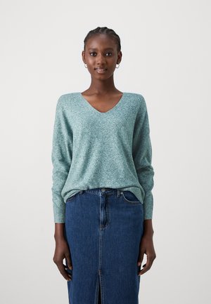 Light green, textured knit sweater with a V-neck and long sleeves, paired with a dark denim skirt featuring a front slit.