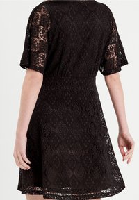 Robe en dentelle noire avec un motif en losanges, manches courtes et un ourlet évasé. Tissu texturé avec une taille cintrée et un dessin en tissage ouvert.