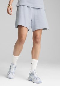 Lichtblauwe, gestructureerde sportshorts met een relaxte pasvorm. Gecombineerd met witte sokken en sneakers, wat een moderne, gelaagde uitstraling geeft.