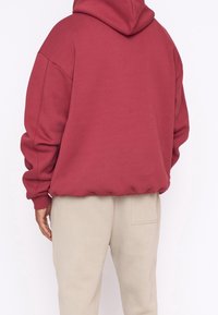 Felpa con cappuccio color bordeaux e vestibilità rilassata, con maniche a costine, abbinata a pantaloni della tuta beige chiaro con una tasca posteriore.