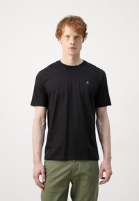 Zwarte katoenen t-shirt met korte mouwen, voorzien van een ronde hals en een klein wit logo op de linkerkant van de borst, gecombineerd met groene broek.
