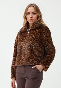 Kurtka z futra ekologicznego w leoparda z wysokim kołnierzem, zapinana na zamek błyskawiczny, o luźnym kroju. Brązowe i czarne kolory tworzą strukturalny wzór.