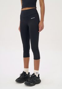 Zwarte capri leggings met een hoge tailleband, een gladde textuur en geen zichtbare patronen, gedragen met zwarte sportschoenen en witte sokken.
