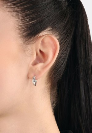 Silberne Creolen mit einem geschwungenen Design und einem kleinen Kristallakzent. Die Oberfläche ist glatt und glänzend, reflektiert das Licht effektiv.