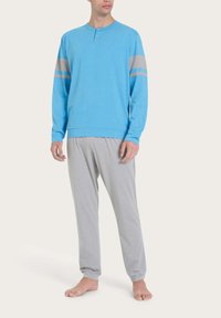 Maglietta leggera a maniche lunghe di colore azzurro con due strisce grigie sulle maniche, abbinata a pantaloni da pigiama grigi. Il tessuto sembra morbido e ha una vestibilità rilassata in tutto.