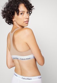 Top sportivo beige con scollatura a U, design senza cuciture e fascia elastica bianca con dettagli del logo "Calvin Klein" in nero.
