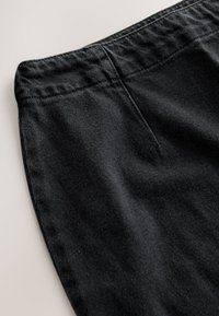 Tessuto di denim nero con superficie testurizzata. Presenta una cintura incassata e dettagli di cuciture visibili. Nessuna tasca visibile.