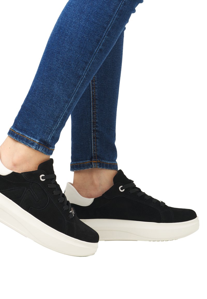 Schwarze Wildledersneaker mit weißen Akzenten, flacher Sohle, abgerundeter Spitze, Schnürdesign und engem Sitz an Jeans, der das Profil des Schuhs betont.