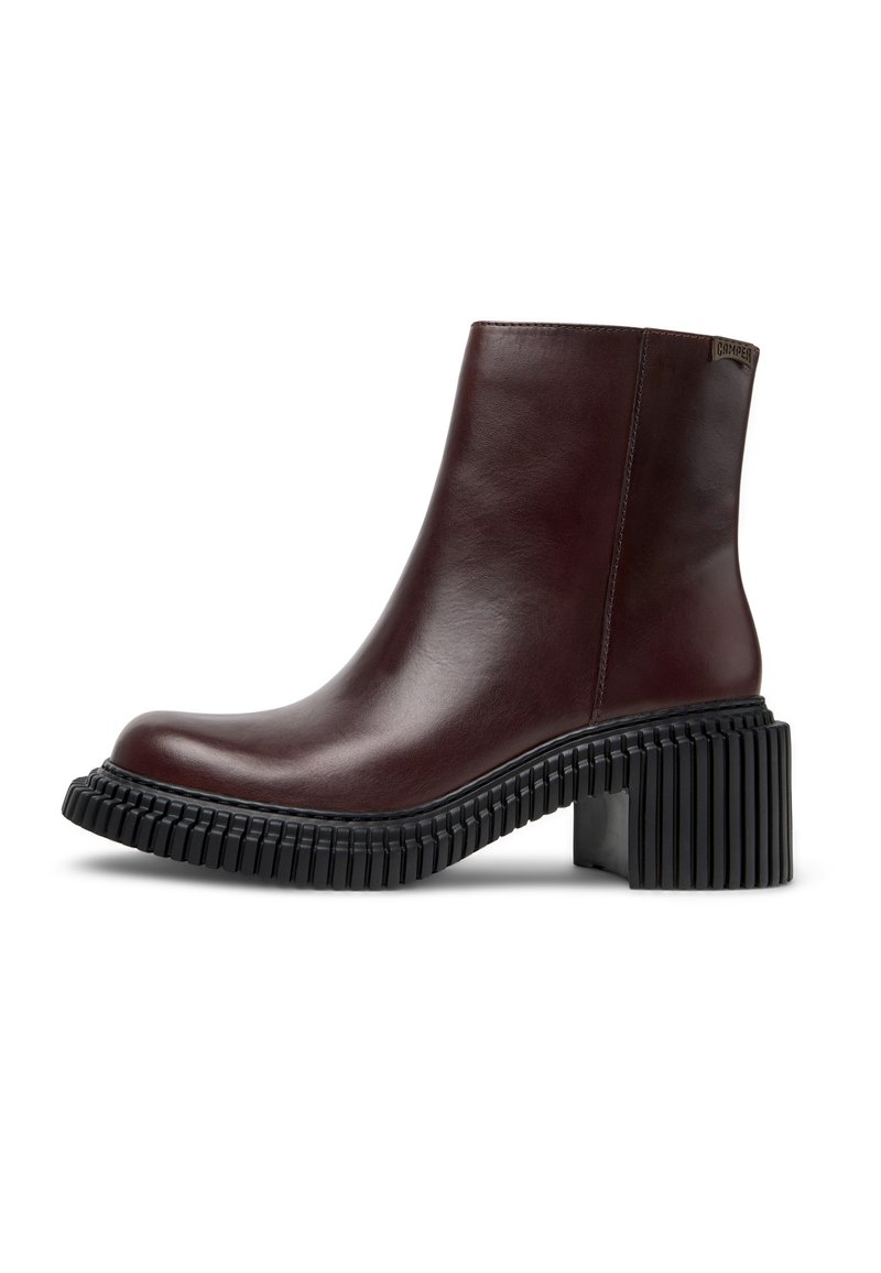 Bota de tobillo de cuero burdeos con punta redondeada, suela de goma negra texturizada y diseño de tacón grueso. Detalle de logotipo en latón en el lateral.