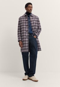 Gepufferter Wolle-Mix-Mantel in Lila und Schwarz, mit Knopfverschluss, Reverskragen, kombiniert mit einem Jeanshemd und lässigen Jeans.