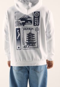 Felpa bianca con grafica navy che presenta il Monte Fuji, fiori di ciliegio e una pagoda, oltre al testo che riporta "GIAPPONE" e "40".