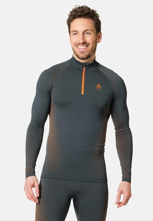 Long-sleeve athletic top in dark gray with orange zip and logo. Features textured fabric and dotted gradient pattern on sleeves.