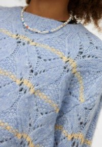 Gaiši zils adīts džemperis ar sarežģītu mežģīņu rakstu, kurā ir dzeltenas svītras. Mīksta tekstūra ar vaļēju piegriezumu un ribotu apkakli.