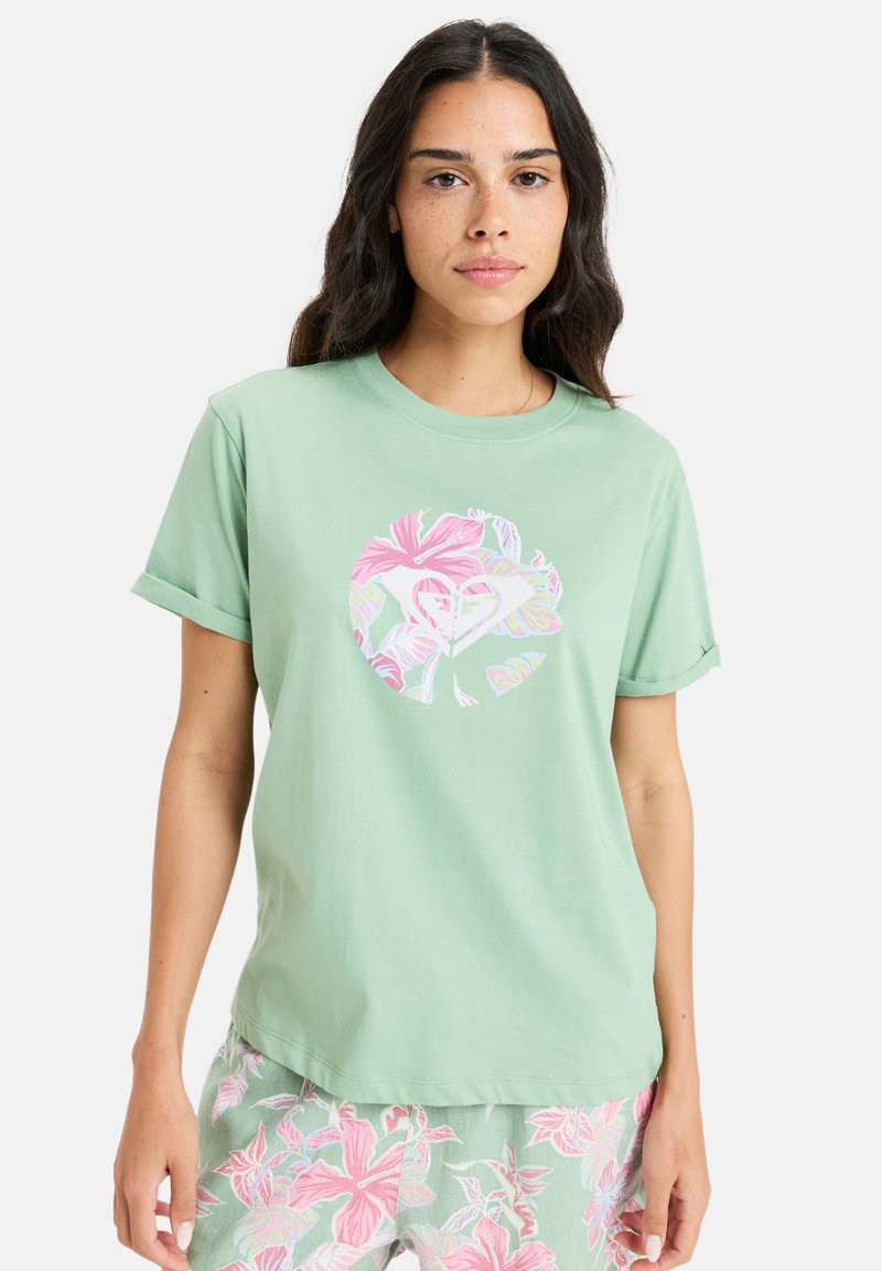 Lys grøn bomulds t-shirt med rullede ærmer og et cirkulært blomstermotiv i pink, hvid og pastelfarver på forsiden.