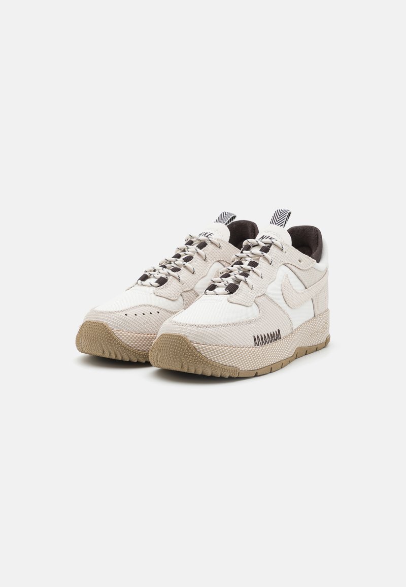 Baskets beiges clairs avec un dessus en maille texturée, des accents blancs contrastants, des lacets à motifs noir et blanc, et une semelle en caoutchouc beige.