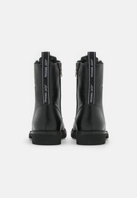 Bottines noires en cuir avec une semelle robuste, dotées d'une fermeture éclair latérale et d'une languette en tissu contrastant. Design simple et fonctionnel.