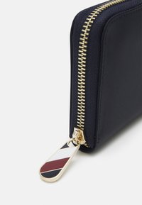 Navy fabric wallet with a gold zipper, featuring a striped zipper pull in red, white, and black. Smooth texture, rectangular shape.