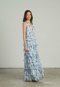 El vestido largo azul con flores presenta un escote en V profundo, capas de volantes en niveles y una cintura ajustada, hecho de una tela ligera con una textura suave.