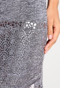 Tessuto a maglia grigia con un motivo openwork esagonale e accenti metallici. Inquadratura ravvicinata con una mano posizionata di lato.