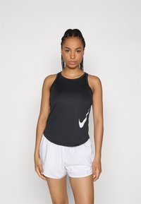 Zwarte sportieve tanktop met een gebogen zoom en wit Nike-logo aan de linkerkant, gecombineerd met witte sportshorts. Glad, lichtgewicht materiaal.