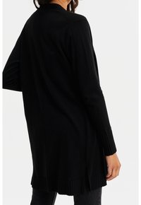 Svart långärmad kardigan med ribbade ärmslut och nederkant, med sidoklyftor för lätt rörelse, tillverkad i ett mjukt material.