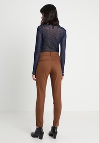 Top de manga larga azul marino semitransparente con lunares, combinado con pantalones marrones ajustados. Botines negros de tobillo completan el conjunto.